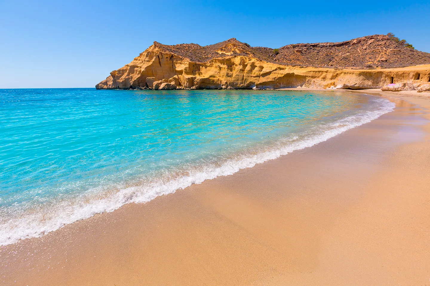 Cala de arena dorada y agua turquesa al pie de un acantilado
